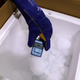 An employee wearing a bright blue insulated glove displays the temperature of -80.6 degrees celsius for a package containing a foam container filled with dry ice inside a cold storage facility in Gurugram, India.